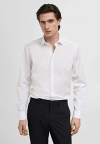 Witte lange mouw blouse met een puntkraag en knopenrij, gecombineerd met zwarte broek, die een slanke, nauwsluitende pasvorm laat zien.