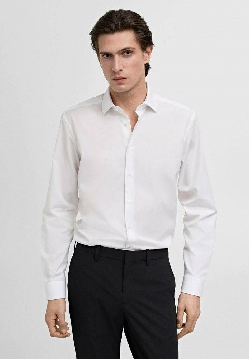 Witte lange mouw blouse met een puntkraag en knopenrij, gecombineerd met zwarte broek, die een slanke, nauwsluitende pasvorm laat zien.