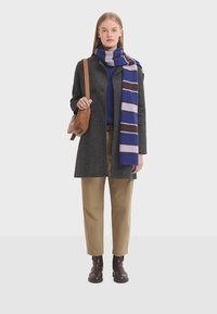 Gray wool coat with black buttons, blue sweater, striped purple and blue scarf, beige trousers, brown leather bag, and brown ankle boots.