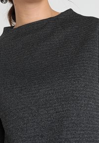 Suéter negro de textura que presenta un cuello alto y un ajuste suave y ligeramente holgado. La tela tiene un sutil patrón tejido que añade profundidad.