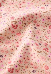 Light pink fabric with a small floral pattern featuring red, purple, and brown flowers and leaves, shown with gentle folds.