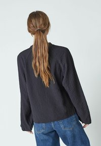 Maglietta nera a maniche lunghe con una vestibilità morbida, caratterizzata da un colletto rotondo e spalle cadenti. Indossata con jeans in denim blu.