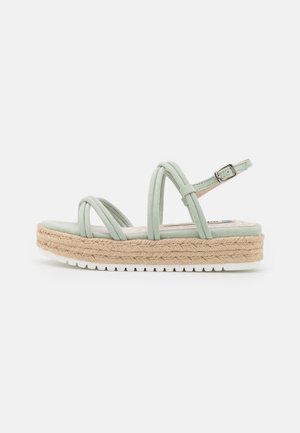 Sandale à plateforme vert clair avec semelle en jute tressée, trois brides rembourrées et boucle de cheville réglable sur fond blanc.