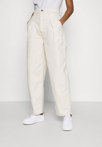 Ljusbeige vida byxor i denim, med framfickor, knäppning med knapp och sidofickor, tillsammans med vita sneakers.