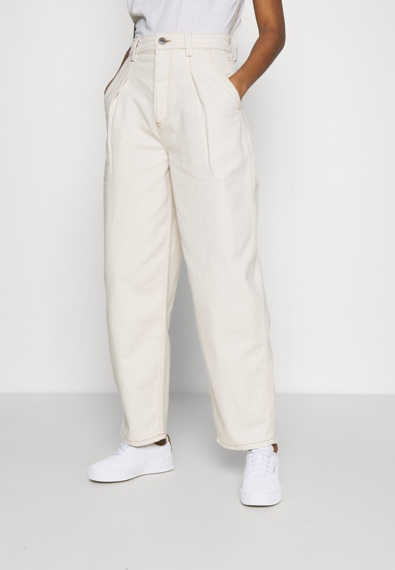 Ljusbeige vida byxor i denim, med framfickor, knäppning med knapp och sidofickor, tillsammans med vita sneakers.