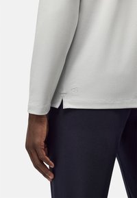 Lichtgrijze longsleeve shirt met een ronde halslijn en zijsplitten, gecombineerd met donkerblauwe broek. Het materiaal lijkt glad met een gestructureerde afwerking.