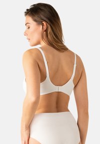 Soutien-gorge blanc en coton avec des bretelles réglables, une texture lisse et une fermeture à crochets et œillets au dos. Design simple et fonctionnel.