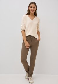 Beige stickad tröja med V-ringning och rullade ärmar, tillsammans med bruna elastiska sweatpants med justerbart snöre och sidofickor.