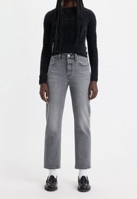 Jean gris de cintura alta con pierna recta, combinados con un top negro de manga larga texturizado y mocasines negros, que llevan calcetines blancos al tobillo.