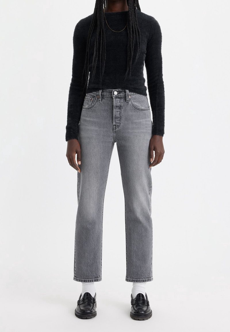 Jean gris de cintura alta con pierna recta, combinados con un top negro de manga larga texturizado y mocasines negros, que llevan calcetines blancos al tobillo.