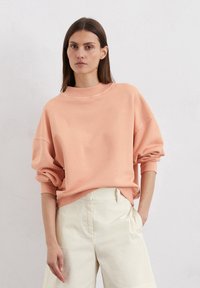 Licht perzikkleurige oversized sweatshirt met een hoge halslijn, brede mouwen en geribde manchetten, gecombineerd met romige wijde broekspijpen.