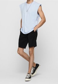 Světle modrý bezrukávový top, černé šortky a černé tenisky. Top má volný střih, zatímco šortky jsou po kolena s jednoduchým designem.
