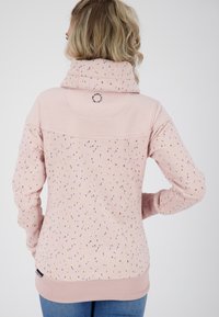 Světle růžová mikina s vysokým límcem, která má posázený vzor v purpurové, žluté a oranžové barvě. Hladké manžety a lem. Jemný detail loga.