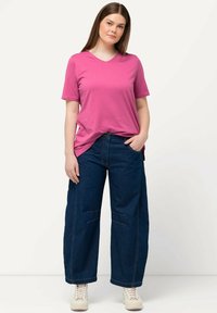 Rosa Baumwoll-V-Ausschnitt-T-Shirt, kombiniert mit weit geschnittenen dunkelblauen Jeans mit Nähdetails, getragen mit hellen Sneakers.