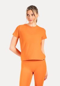 Camiseta deportiva naranja de manga corta hecha de tela suave con cuello redondo, combinada con leggings ajustados a juego. Diseño minimalista.