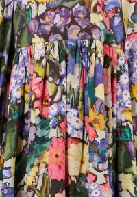 Jasna tkanina sukienki w kwiaty z dużymi, wielokolorowymi kwiatami w odcieniach fioletu, różu, żółci i bieli, z marszczeniami i zielonymi liśćmi.