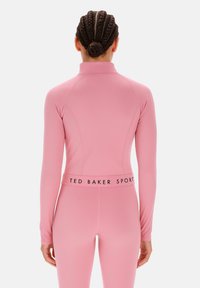 Hosszú ujjú, testhez simuló felső és leggings sima rózsaszín anyagból, magas gallérral és márkázott derékpánt részletezéssel.