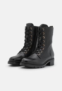 Par de botas de cuero negras de cordones hasta el tobillo con cremalleras laterales y tacones bajos gruesos sobre un fondo blanco.