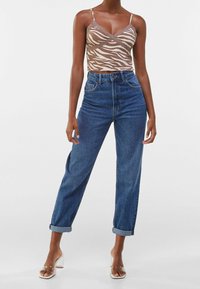 Top corto a rayas con tonos marrones y blancos, con acentos de encaje, combinado con jeans de mezclilla azul de tiro alto, con puños doblados, y sandalias de tacón transparente.