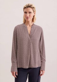 Blouse met lange mouwen in een bruin-crème geometrisch patroon. Heeft een V-hals en een ontspannen pasvorm met een zacht, lichtgewicht stof.