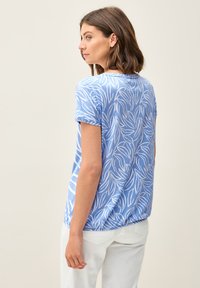 Haut bleu clair à manches courtes avec un motif de feuilles blanches, encolure arrondie et coupe décontractée. Tissu doux avec une texture lisse, associé à un pantalon blanc.