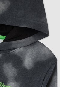 Felpa grigia scura con fodera interna nera e un sottile motivo tie-dye, con una grafica neon verde parziale vicino al bordo inferiore sinistro.