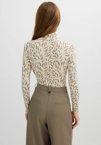 Top de manga larga en color crema con un estampado de hojas marrones. Combinado con pantalones de talle alto en verde oliva que cuentan con bolsillos traseros y cierre de botón.