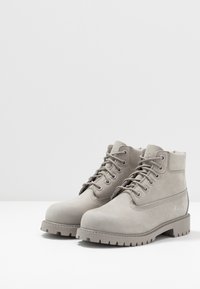 Stivali alla caviglia in suede grigio con occhielli in metallo, design con lacci, colletto imbottito, suola in gomma rugged e logo sottile sul lato.