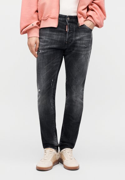 Μαύρα τζιν από denim με ξεθωριασμένο φινίρισμα, φθαρμένες λεπτομέρειες και στενή εφαρμογή. Συνδυασμένα με ανοιχτόχρωμα αθλητικά παπούτσια και ροζ φούτερ.