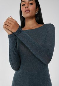 Langarm, figurbetontes Oberteil aus dunkelblauem Strickstoff mit weicher Textur. Verfügt über einen weiten Halsausschnitt und schmale Ärmel. Dezente gepunktete Details.