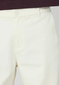 Pantalon en coton blanc avec une texture lisse, doté d'une fermeture à un bouton et de poches latérales, conçu pour un look ajusté.