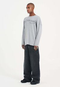 Gray ribbed long-sleeve shirt with graphic design on the chest, paired with wide-leg black jeans and black footwear.