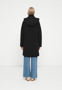 Black hooded coat with a straight cut, soft texture, and long sleeves, paired with wide-leg blue denim jeans and light-colored footwear.