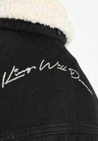 Černá džínová bunda s bílým kožíškovým límcem a výšivkou na zádech. Nápis zní „Keep Well Done“ v kurzívním stylu.