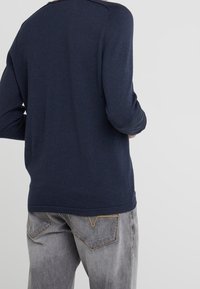 Chemise à manches longues bleu marine avec un col rond, une texture douce et une coupe légèrement ajustée, associée à un jean gris clair avec des coutures jaunes.