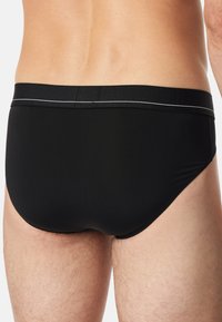 Sorte herresvømmebukser med en struktureret talje, der har en tynd hvid accentlinie. Glat stof, tætsiddende design og minimal dækning.