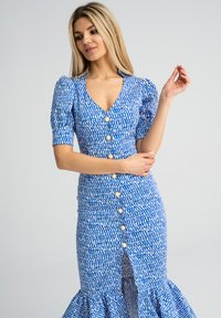 Abito blu con motivo, maniche corte a sbuffo, scollatura a V profonda, chiusura con bottoni anteriori e orlo arricciato. Bottoni decorativi sono chiaramente visibili.