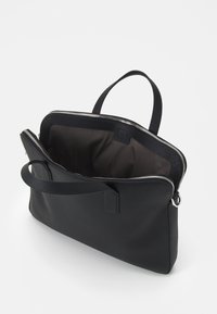 Czarna skórzana torba na laptopa z teksturowanym wykończeniem, zamknięciem na zamek i jednym uchwytem. Wnętrze wyłożone ciemnym materiałem.
