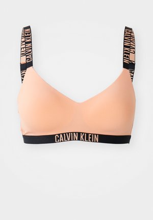 Calvin Kleini bralette pehmeast virsiku värvi kangast, mille pind on sile. Omab musta logo-trükiga rihmu ja vastavat elastset aluspõhja.