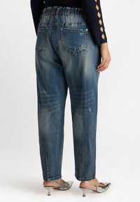 Jeans de mezclilla con un lavado azul claro, cinturilla elástica, corte relajado y sutiles detalles desgastados. Terminados con dos bolsillos traseros.
