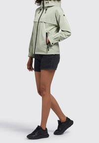 Jasnozielona wodoodporna kurtka na suwak z regulowanym kapturem i czarnymi akcentami. W zestawie z czarnymi szortami dżinsowymi i czarnymi tenisówkami.