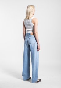 Lichtblauwe wijde jeans met een hoge taille, gemaakt van denim. Heeft subtiele stiksels, twee achterzakken en een logo-patch op de tailleband.