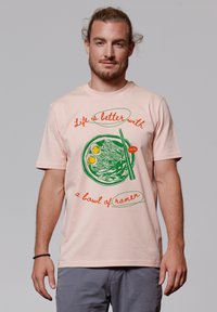 Lichtroze katoenen t-shirt met een groene kom ramen grafiek met twee eieren, aangevuld met rode en groene tekst in een casual lettertype.