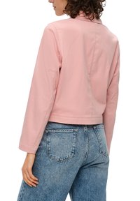 Rosa cropped Jacke mit langen Ärmeln, aus einem glatten Stoff gefertigt. Kombiniert mit hellblauen, hochgeschnittenen Jeans mit Gesäßtaschen.