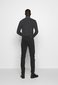 Camisa de manga larga a rayas negra y gris con cuello alto, combinada con pantalones ajustados negros y zapatos negros, vista desde atrás.