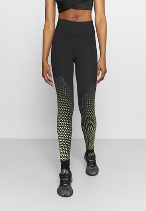 Leggings noirs avec des motifs géométriques jaunes et blancs passant de formes triangulaires à circulaires, design taille haute et tissu extensible.