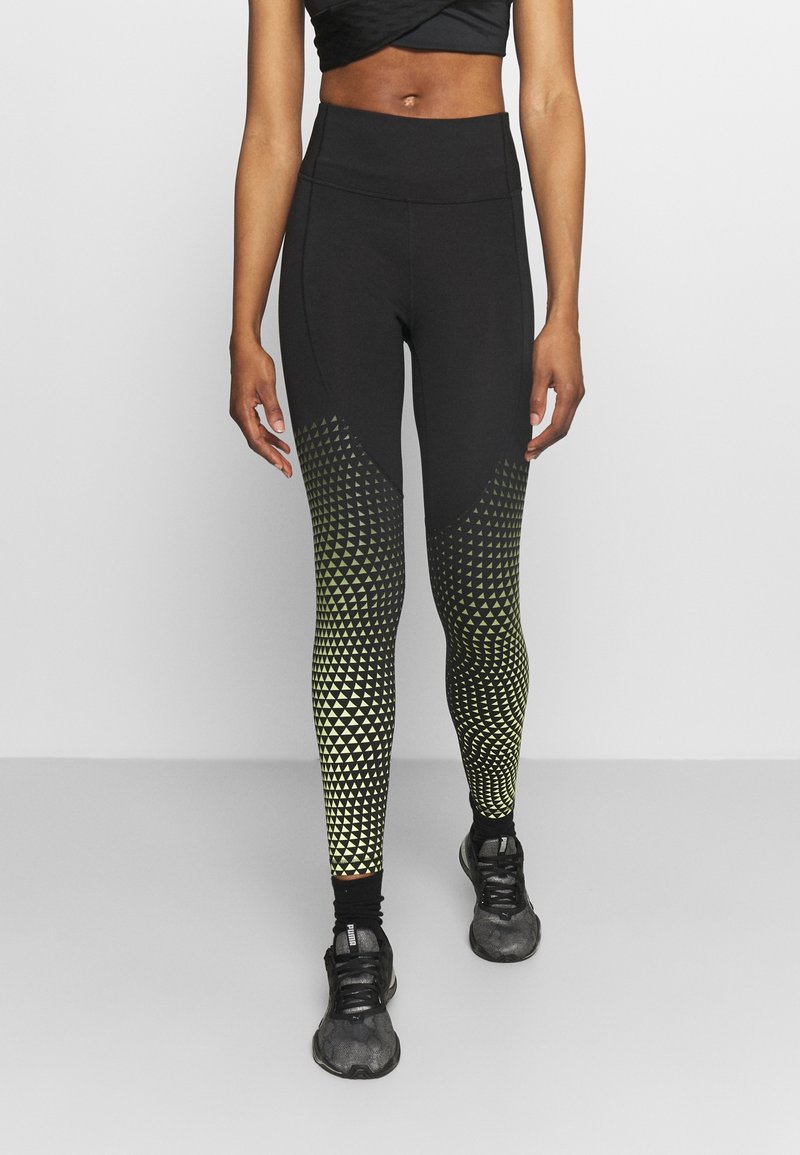 Leggings neri con motivi geometrici gialli e bianchi che si trasformano da forme triangolari a circolari, design a vita alta e tessuto elasticizzato.