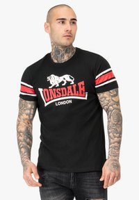 T-shirt in cotone nero con logo Lonsdale bianco e rosso, maniche corte con strisce rosse e bianche, vestibilità standard e scollo rotondo.