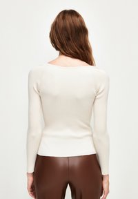Top à manches longues côtelé en beige clair avec un décolleté en cœur. Design ajusté et texture douce, associé à un pantalon ajusté marron.