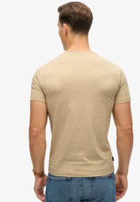 Beige short-sleeve t-shirt in a fitted design, featuring a smooth texture and subtle heather pattern. Located label at left hip.